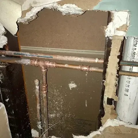 Wall opened up to expose leaking copper supply pipes inside the cavity