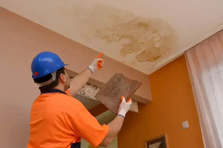Technician in a hard hat checking a ceiling stain left by a roof leak